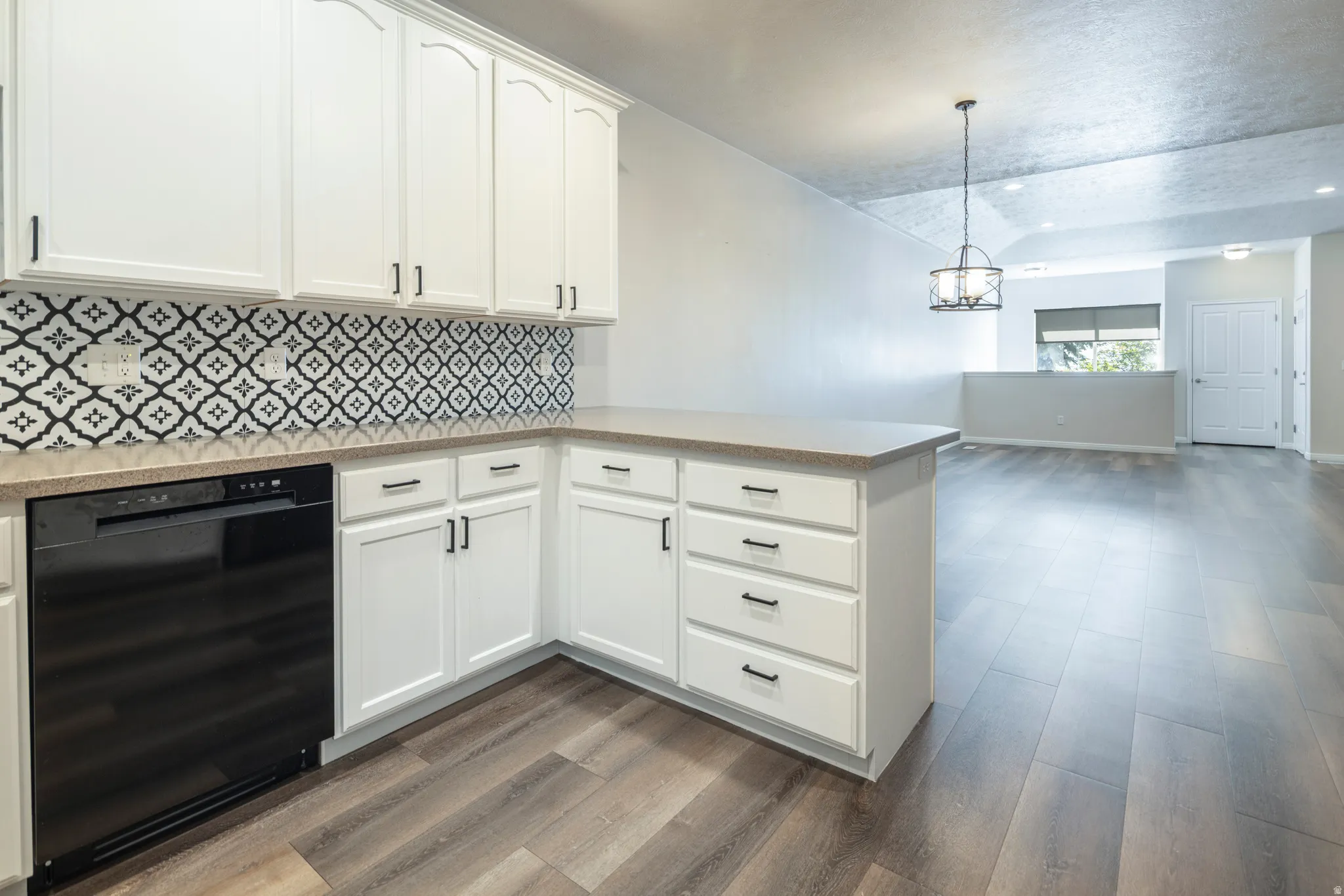 Kitchen featuring black dishwasher, white cabinetry, dark wood finished floors, tasteful backsplash, and a peninsula