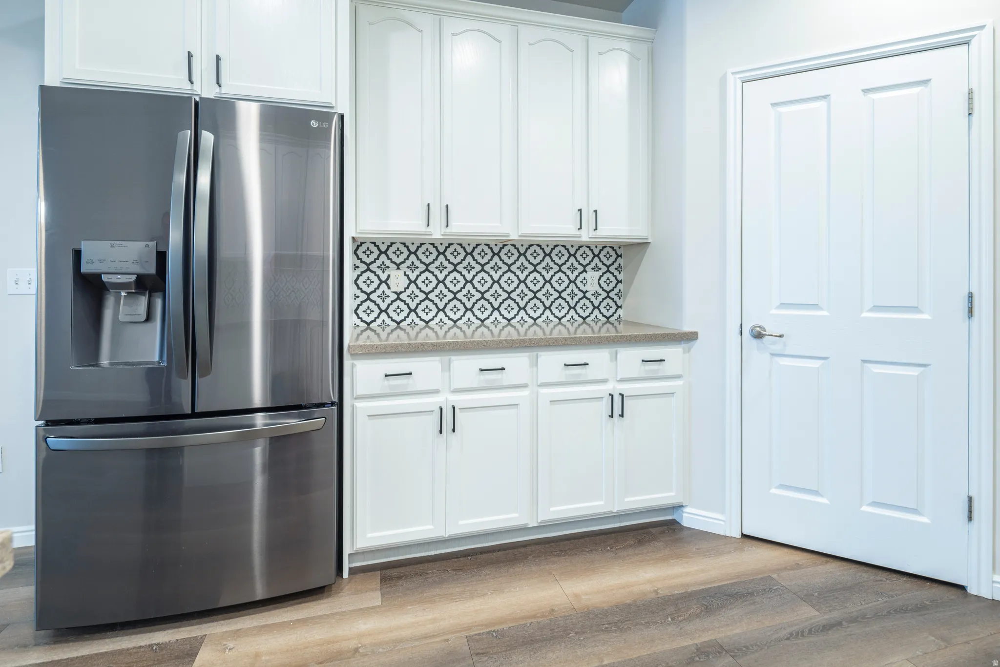 Kitchen with stainless steel fridge with ice dispenser, white cabinets, light wood-style flooring, light stone countertops, and tasteful backsplash