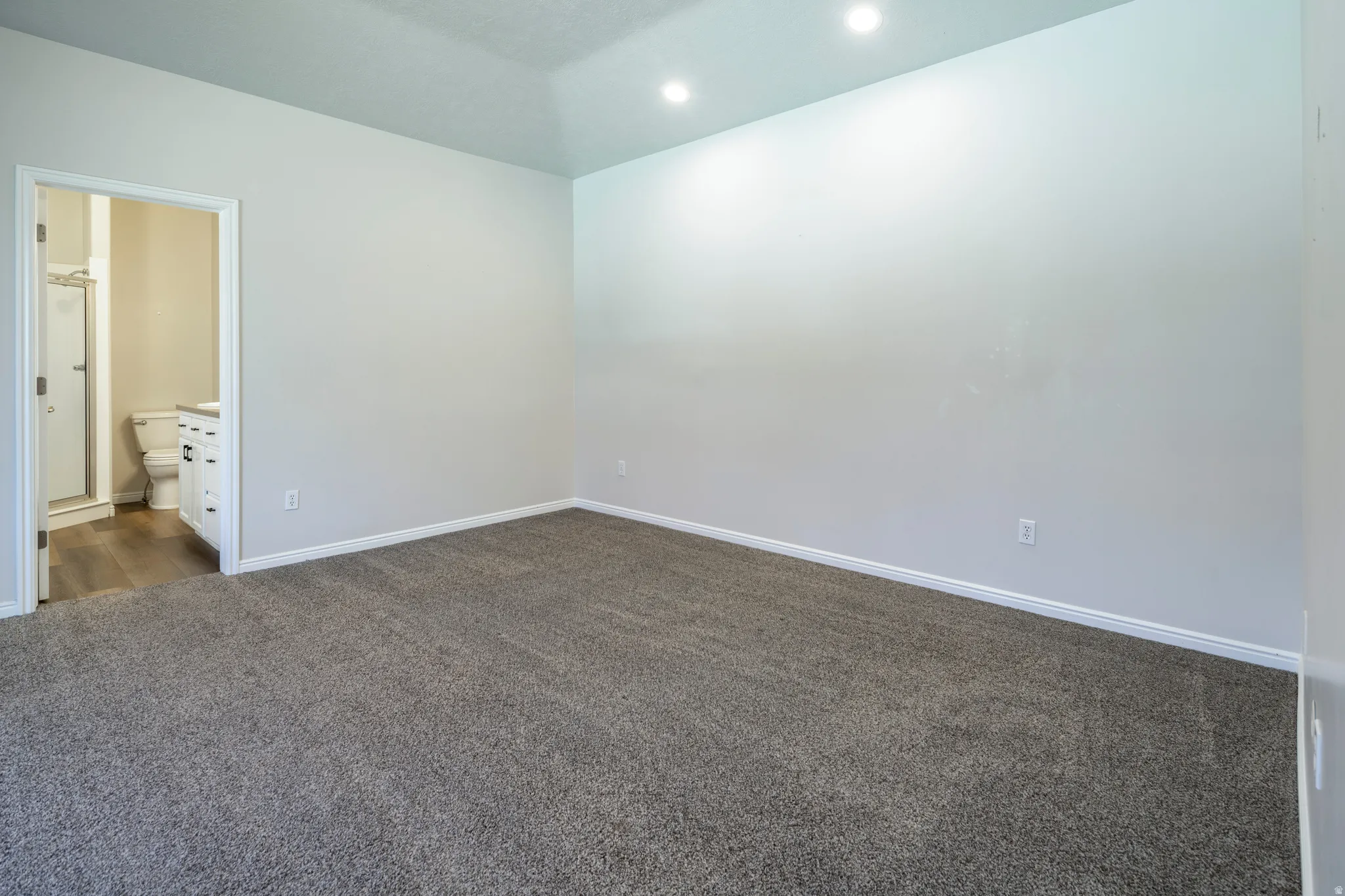 Unfurnished bedroom featuring dark carpet, connected bathroom, and recessed lighting