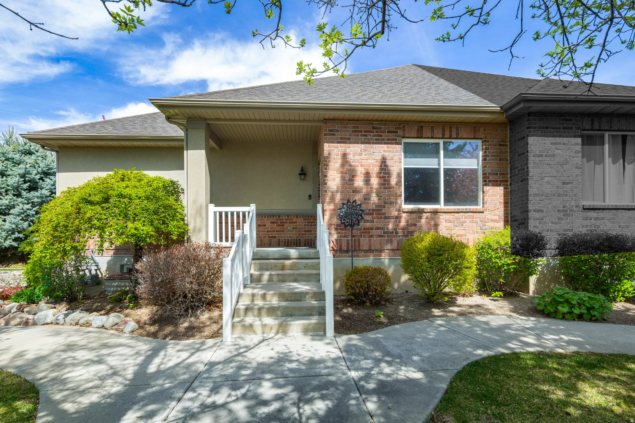 Ranch-style home featuring roof with shingles, a porch, brick siding, and stucco siding