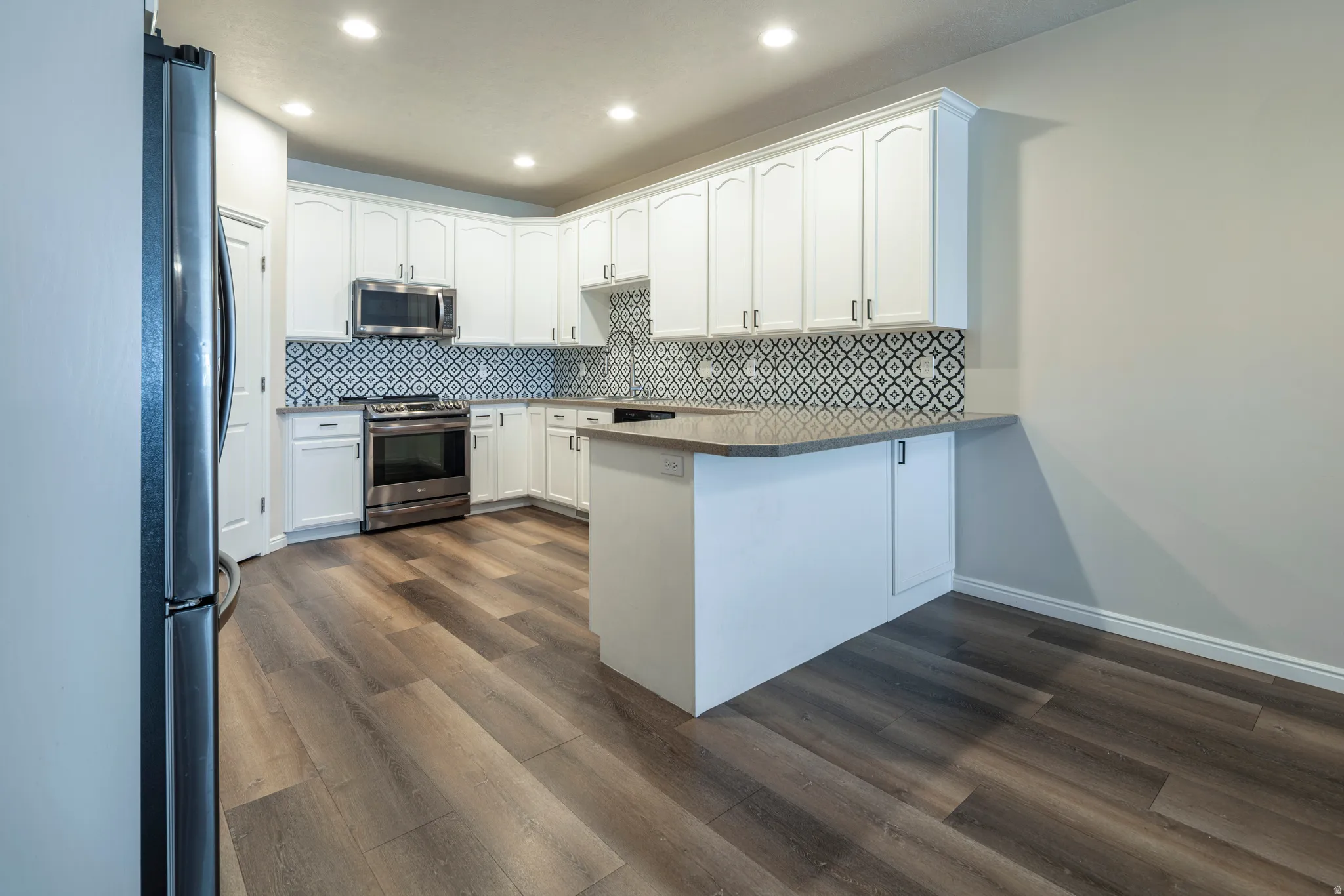 Kitchen featuring white cabinetry, a peninsula, dark wood finished floors, stainless steel appliances, and recessed lighting