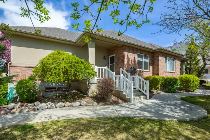 Ranch-style home with a shingled roof, brick siding, covered porch, stucco siding, and a front lawn