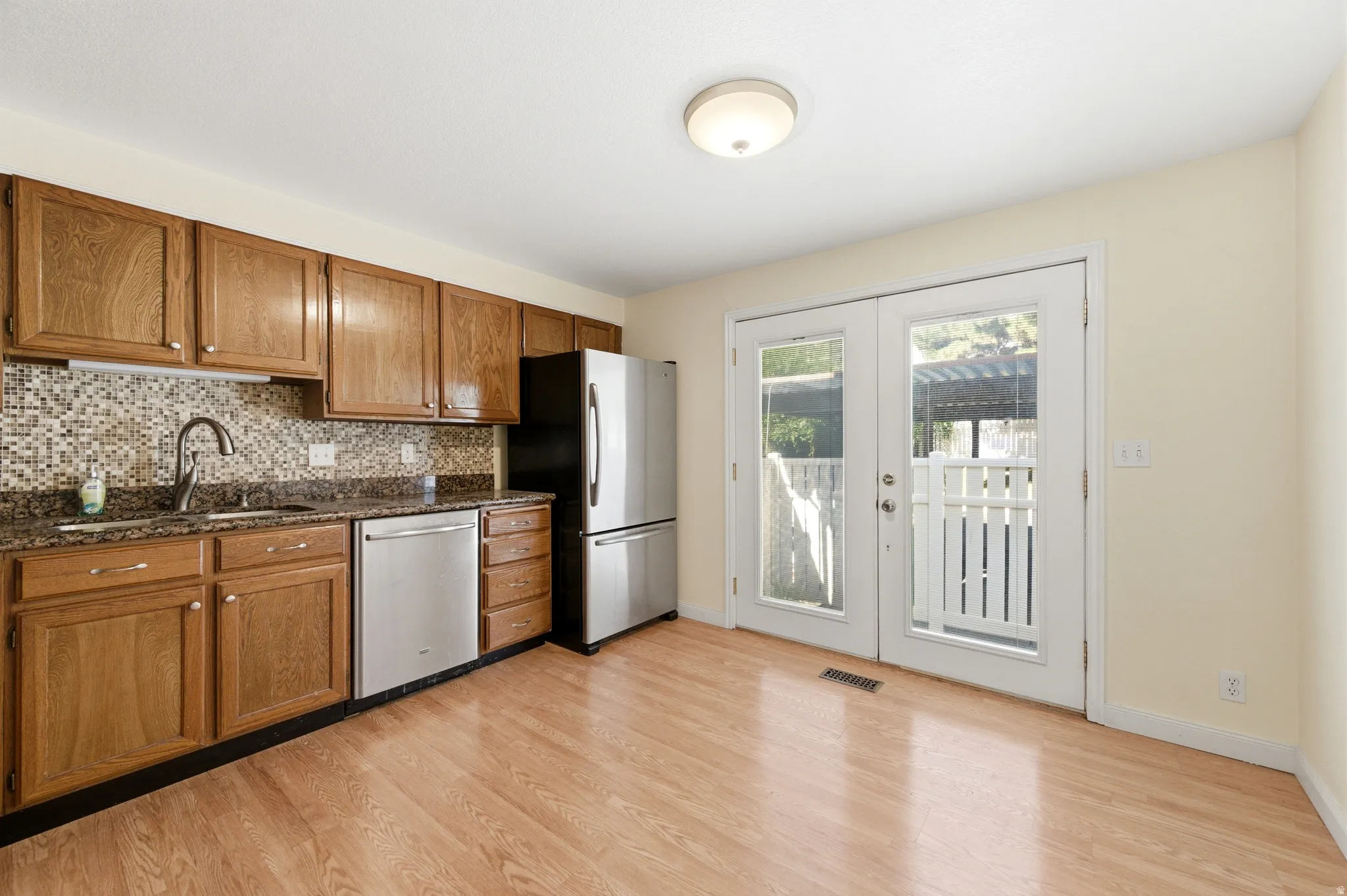 Kitchen with wood finish cabinetry, stainless steel appliances, dark stone countertops, tasteful backsplash, and french doors