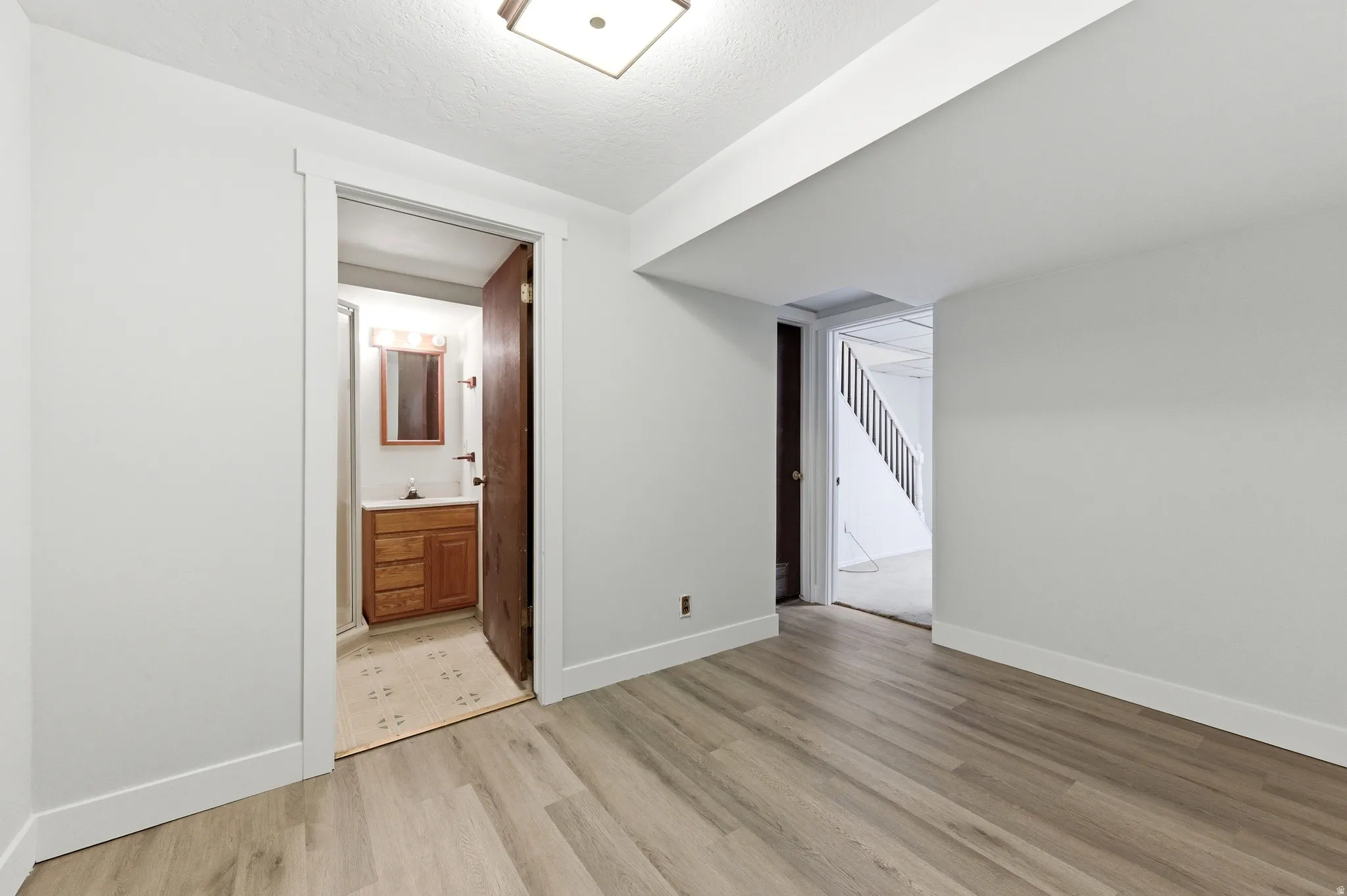 Bedroom with light wood-style flooring, ensuite bath, and a textured ceiling