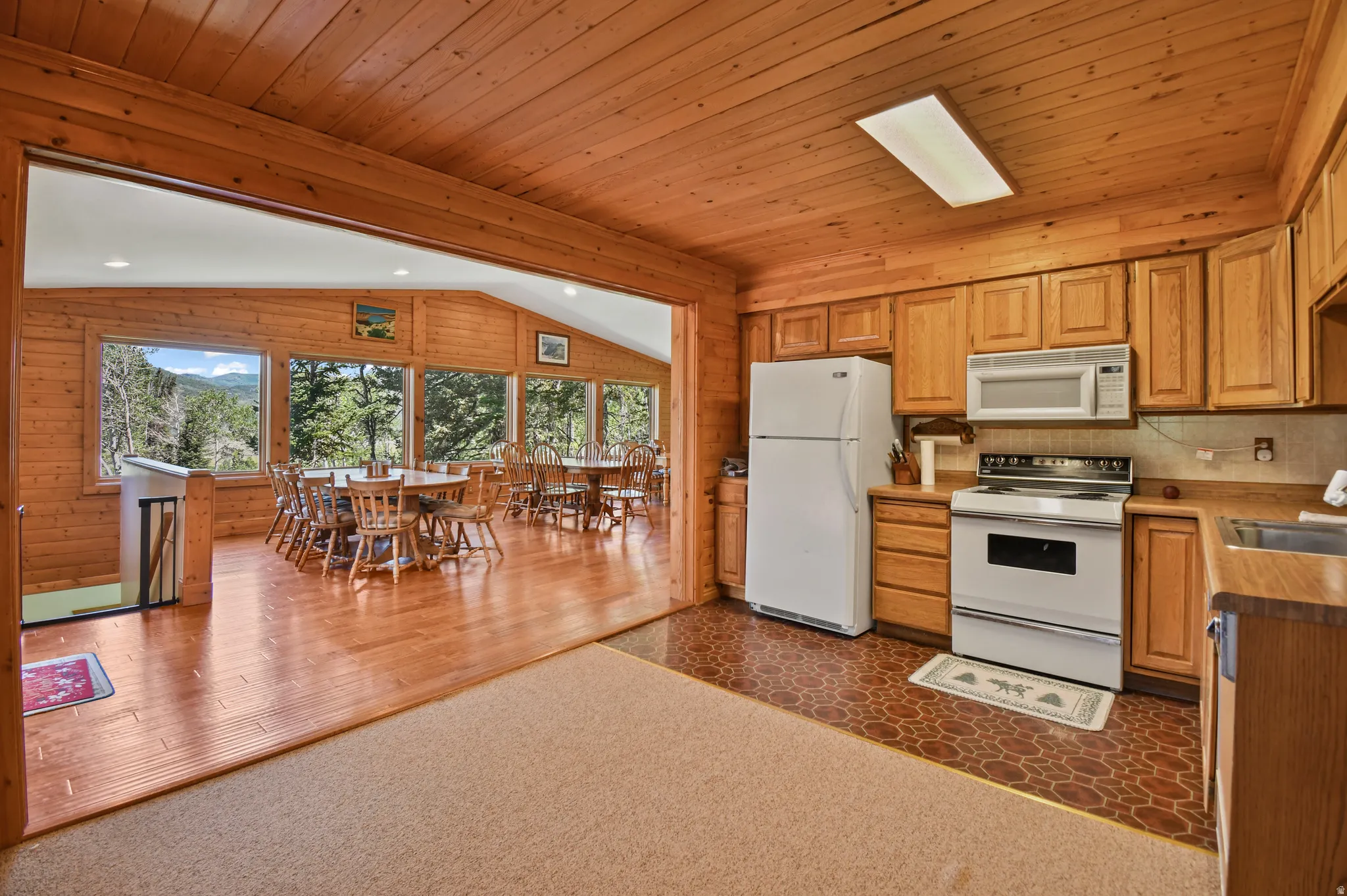 Kitchen with white appliances, wood walls, light countertops, dark colored carpet, and a vaulted wooden ceiling
