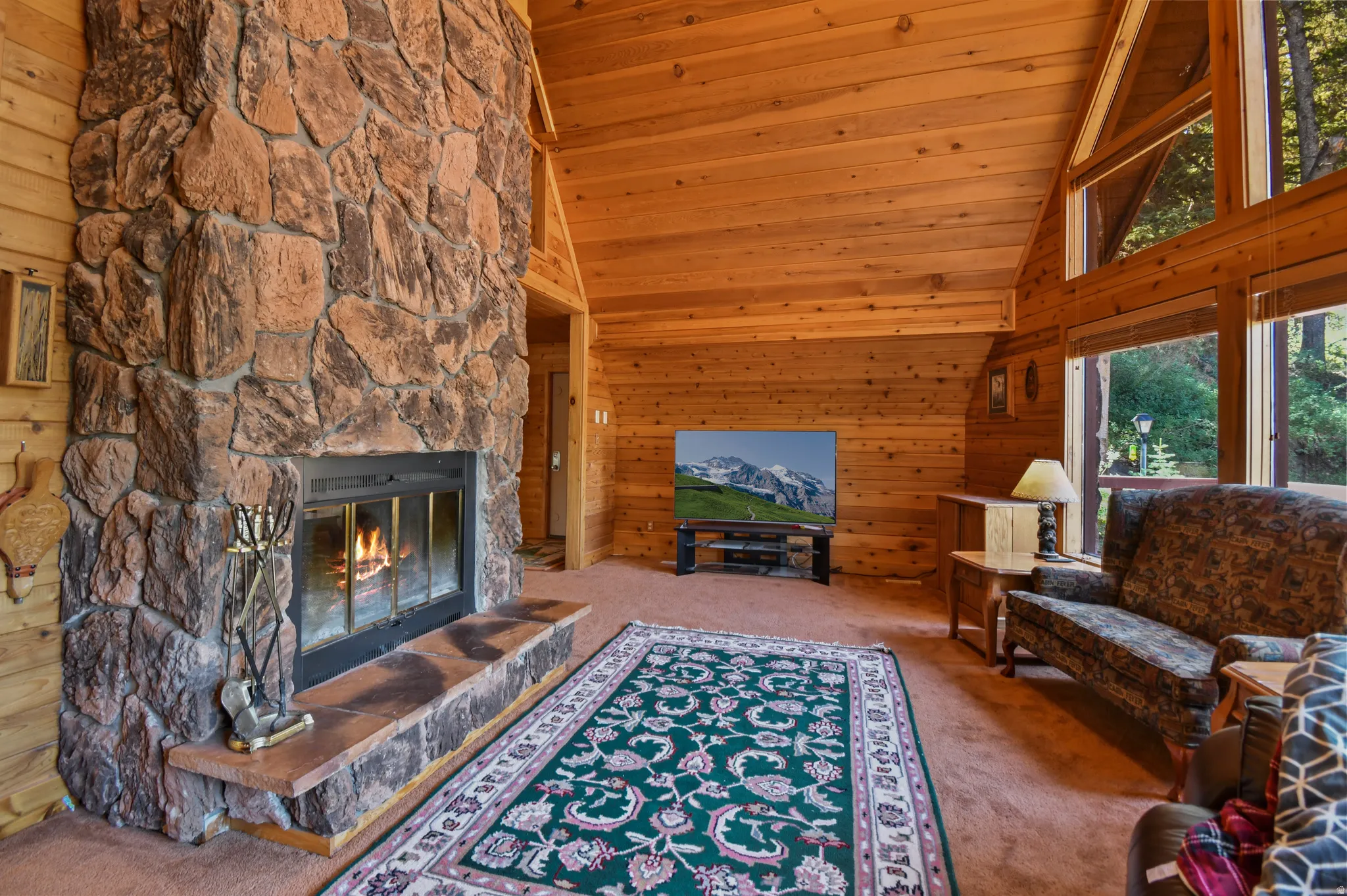 Living room with wooden walls, carpet, a fireplace, and a vaulted wooden ceiling