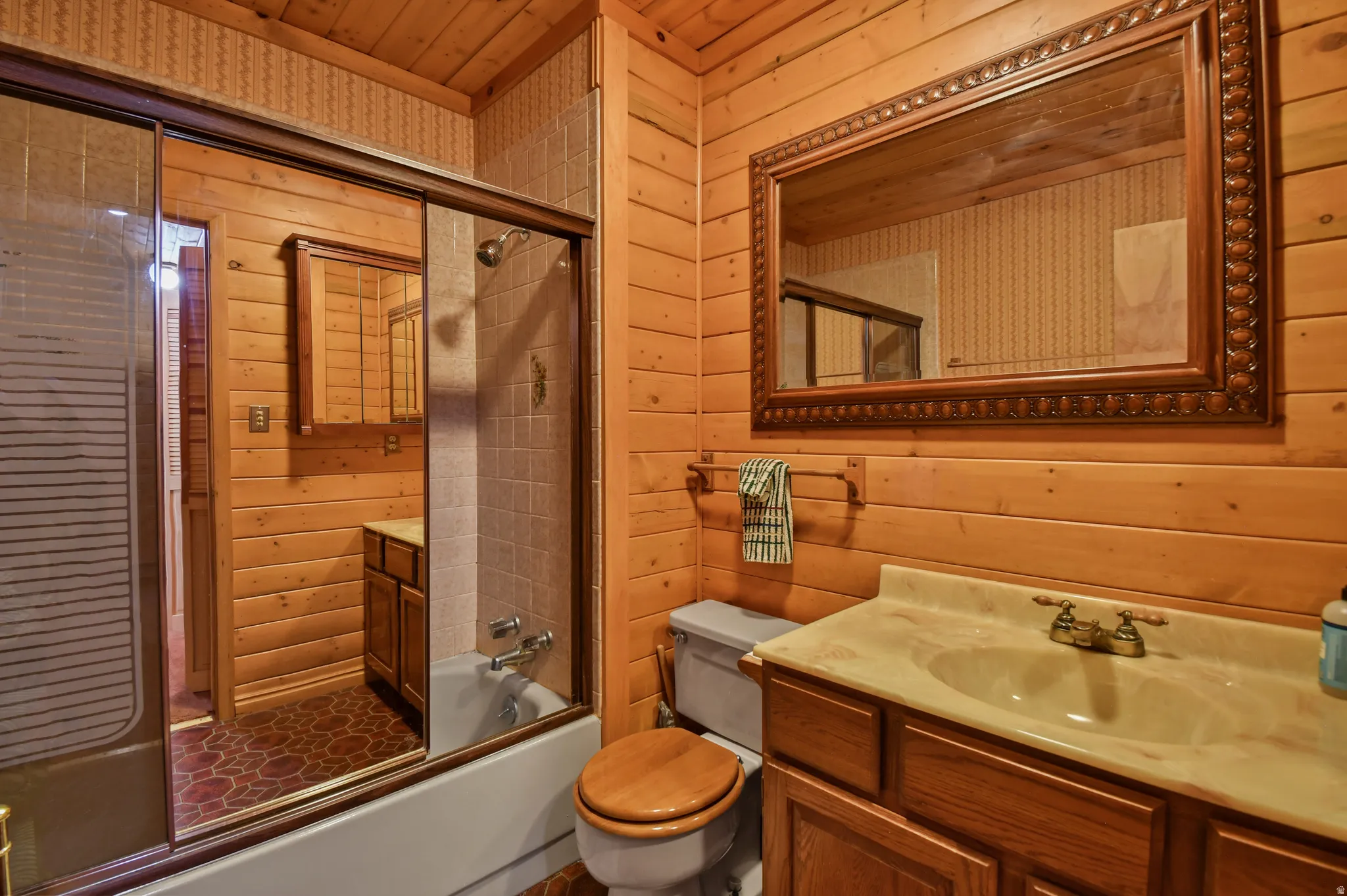 Bathroom featuring wooden walls, vanity, bath / shower combo with glass door, and wood ceiling