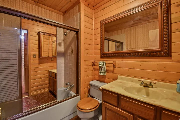 Bathroom featuring wooden walls, vanity, bath / shower combo with glass door, and wood ceiling