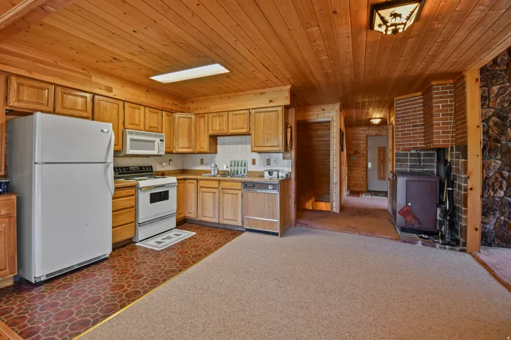 Kitchen featuring white appliances, wood ceiling, dark colored carpet, and light countertops