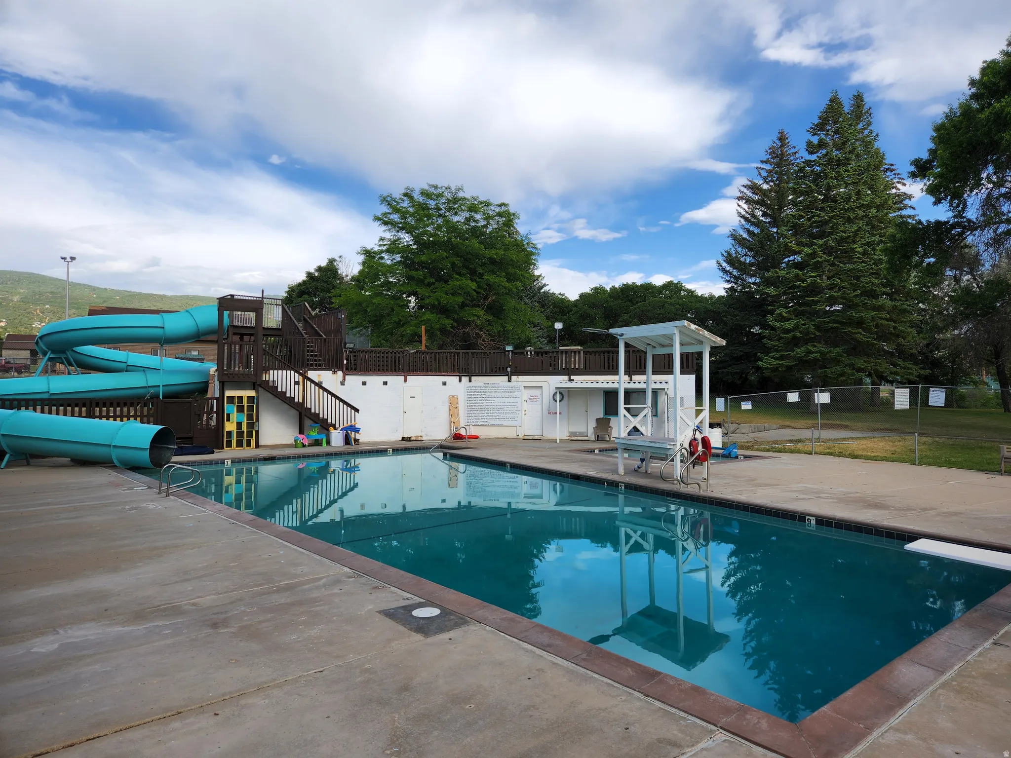 Community pool featuring a water slide, a patio, and a diving board