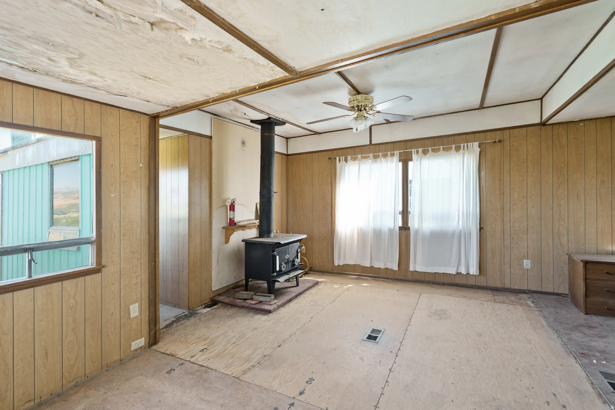 Living area with wood walls, a wood stove, and a ceiling fan