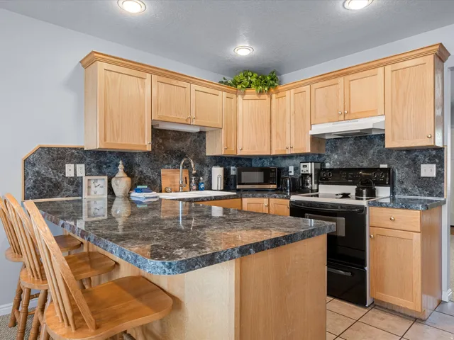 Kitchen with light wood finish cabinets, black electric range oven, a kitchen breakfast bar, a peninsula, and dark countertops