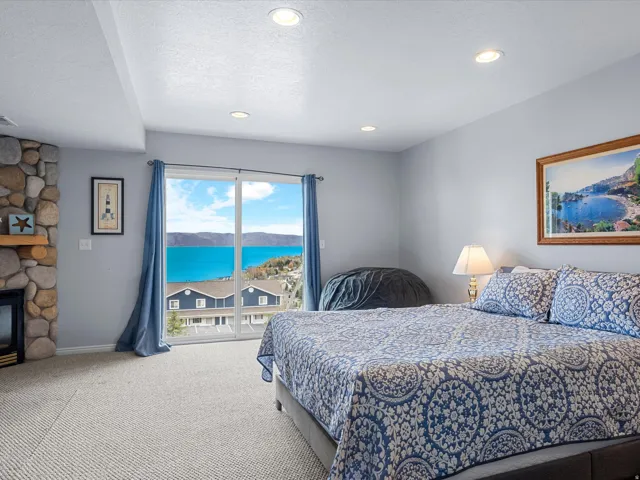 Bedroom featuring a textured ceiling, a stone fireplace, light colored carpet, recessed lighting, and a water and mountain view