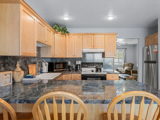 Kitchen with light wood finish cabinetry, black range with electric cooktop, freestanding refrigerator, dark stone countertops, and decorative backsplash