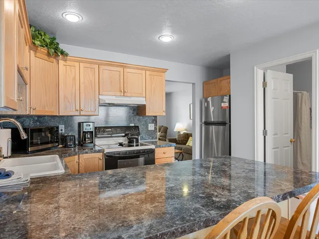 Kitchen featuring stainless steel appliances, backsplash, light wood finish cabinets, a breakfast bar area, and dark stone counters
