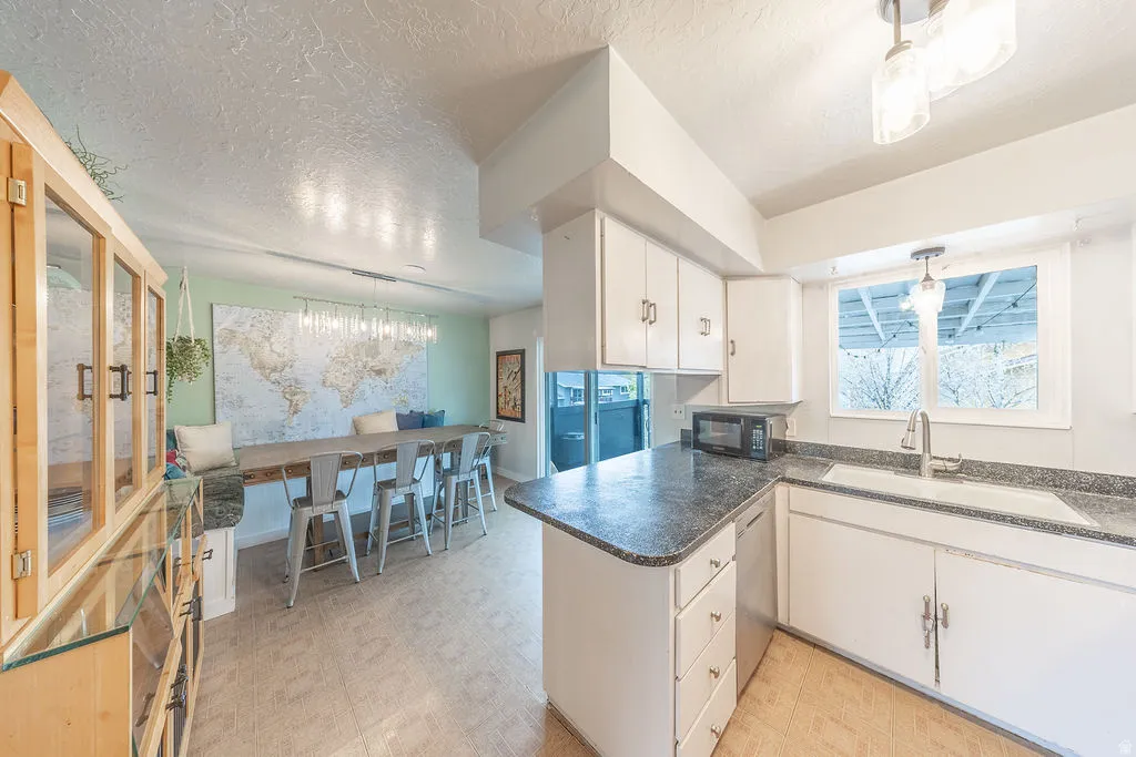 Kitchen with decorative light fixtures, white cabinets, light flooring, a textured ceiling, and dark countertops