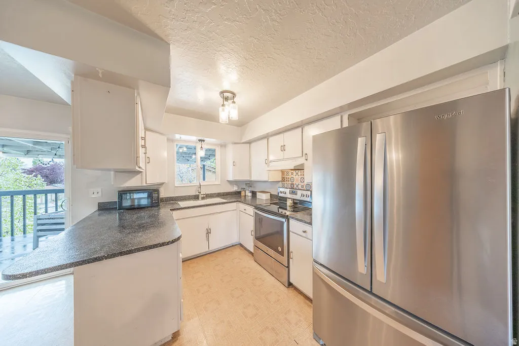Kitchen featuring stainless steel appliances, dark countertops, white cabinets, a peninsula, and light flooring