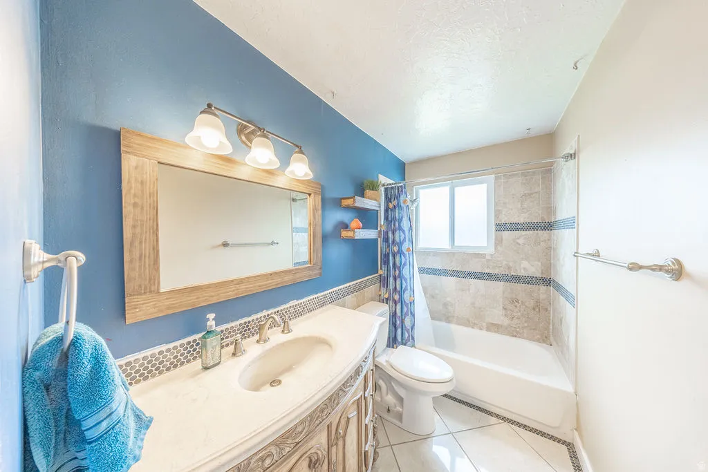 Full bath with vanity, shower / bath combo with shower curtain, light tile patterned flooring, and a textured ceiling