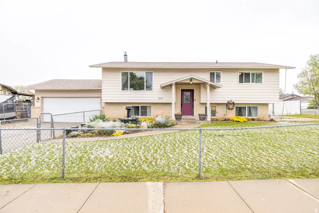Split foyer home featuring brick siding, a garage, a fenced front yard, and driveway