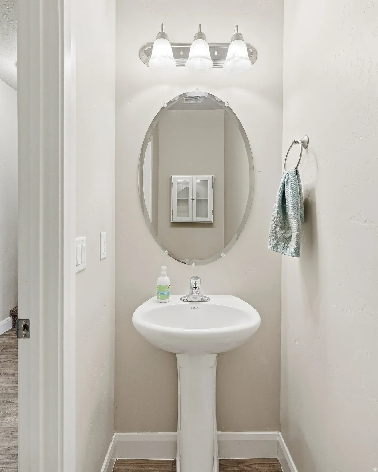 Pedestal sink with a chrome faucet, oval mirror, and a three-light vanity fixture