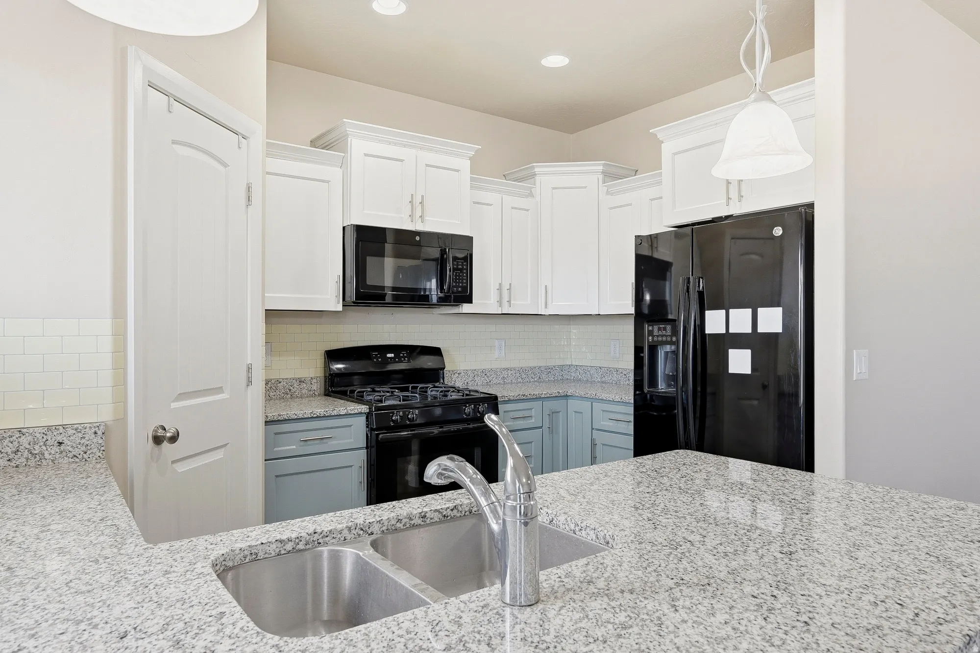 Kitchen featuring light-toned countertops, white upper cabinetry, and a black appliance suite