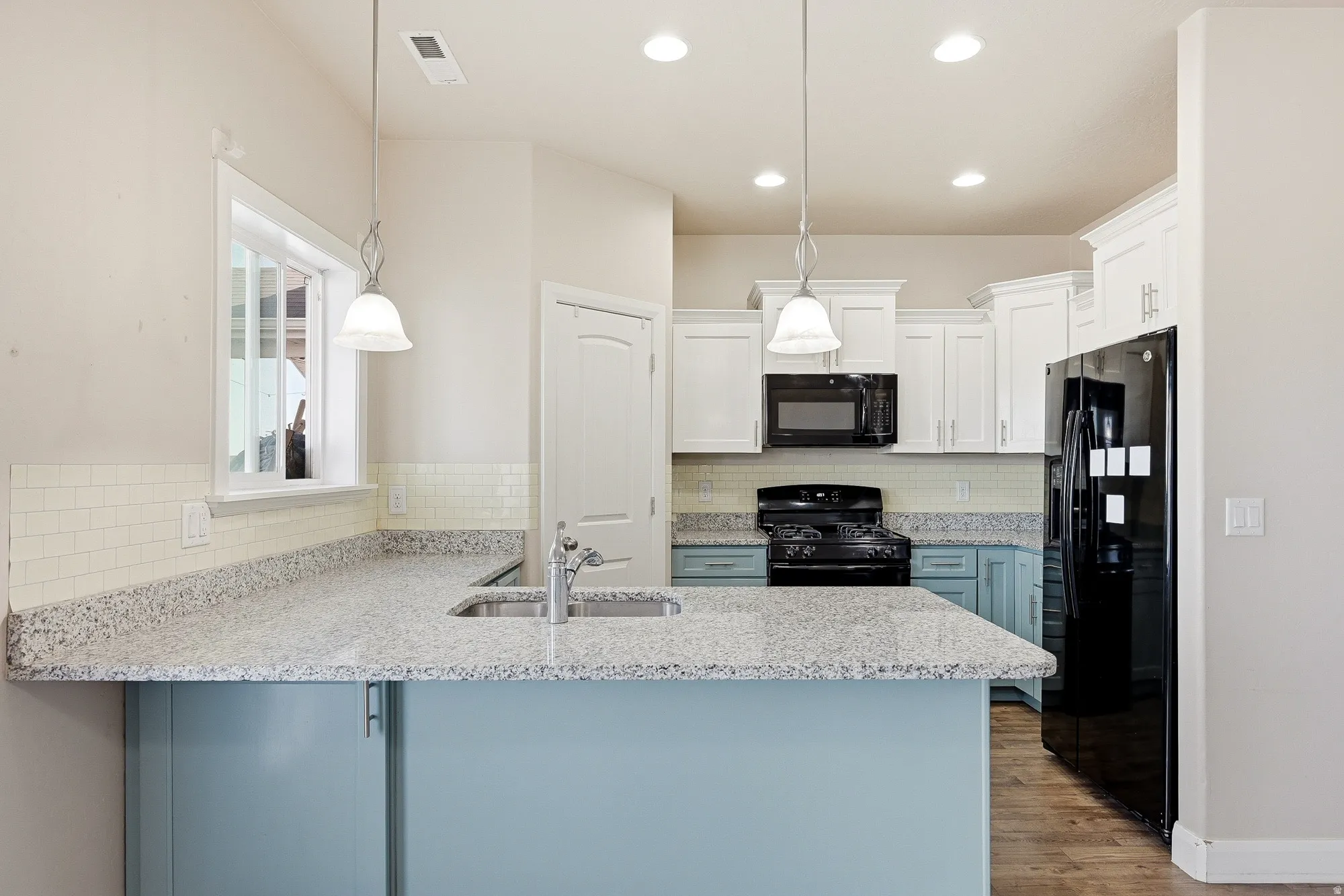 Two tone kitchen featuring light stone countertops, a peninsula, black appliances, hanging light fixtures, and light wood-style flooring