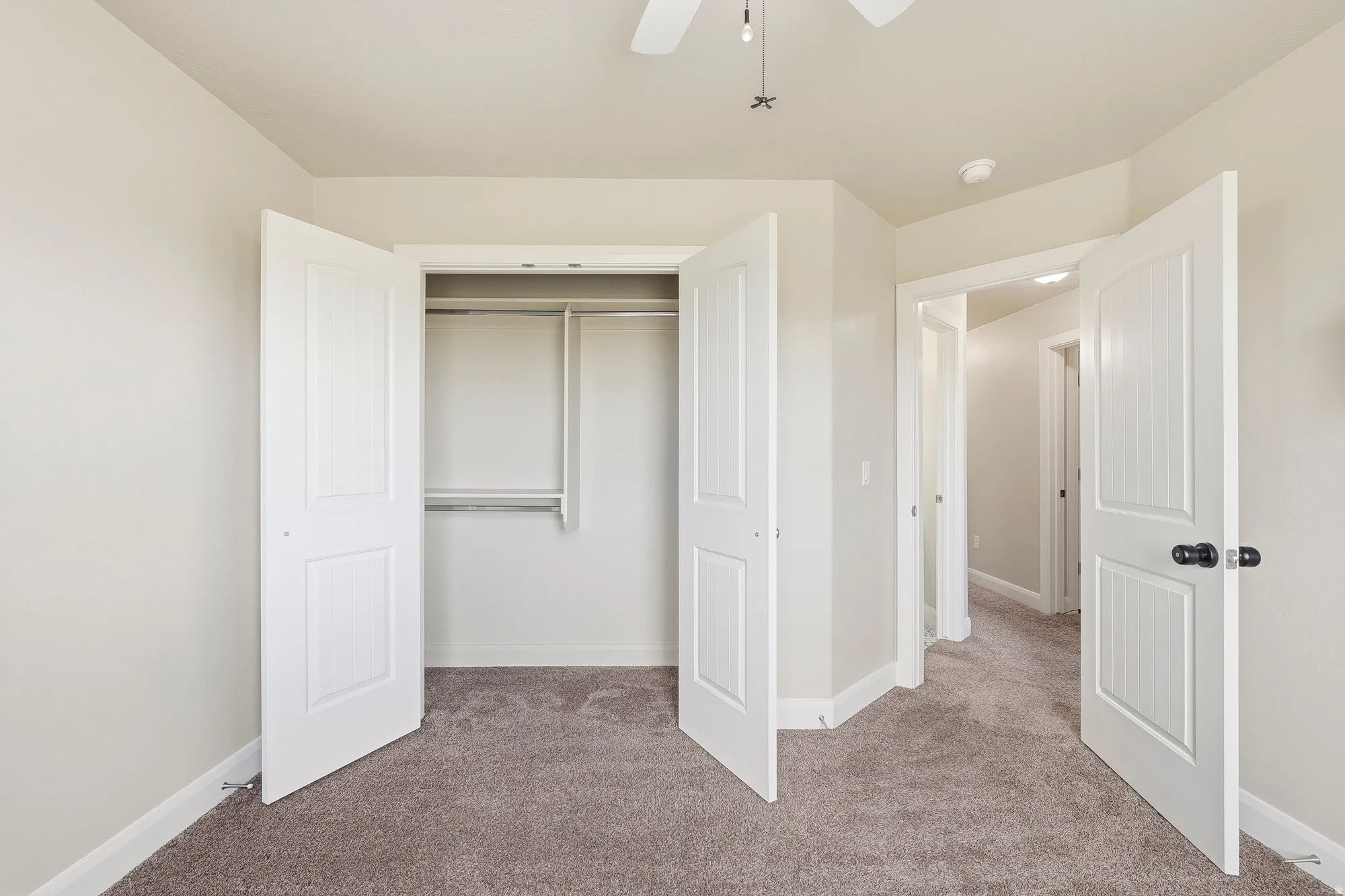 Neutral-toned room with plush carpeting and a ceiling fan