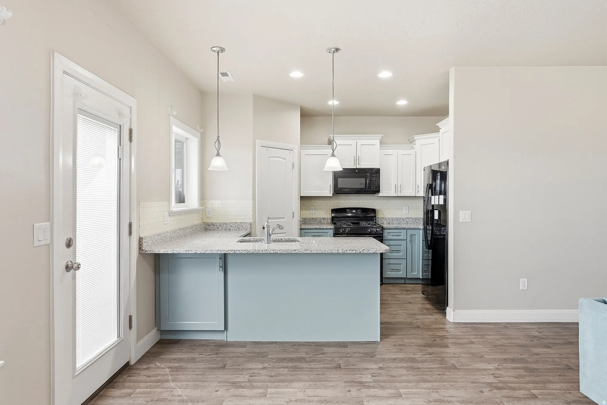 Open-concept kitchen featuring a two-tone cabinetry design, black appliances, wood-finish flooring, and pendant lighting
