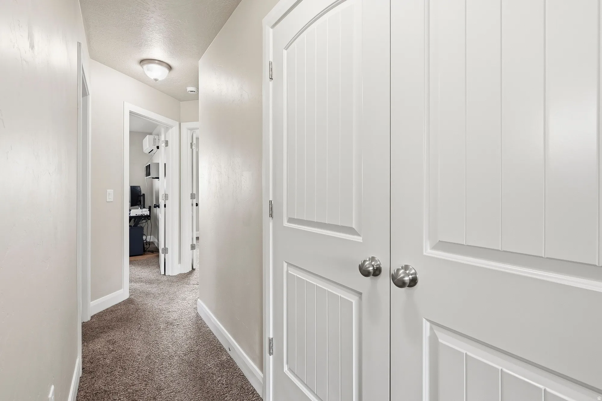 Hallway featuring two white paneled doors with brushed nickel hardware, neutral-toned walls, and carpet flooring