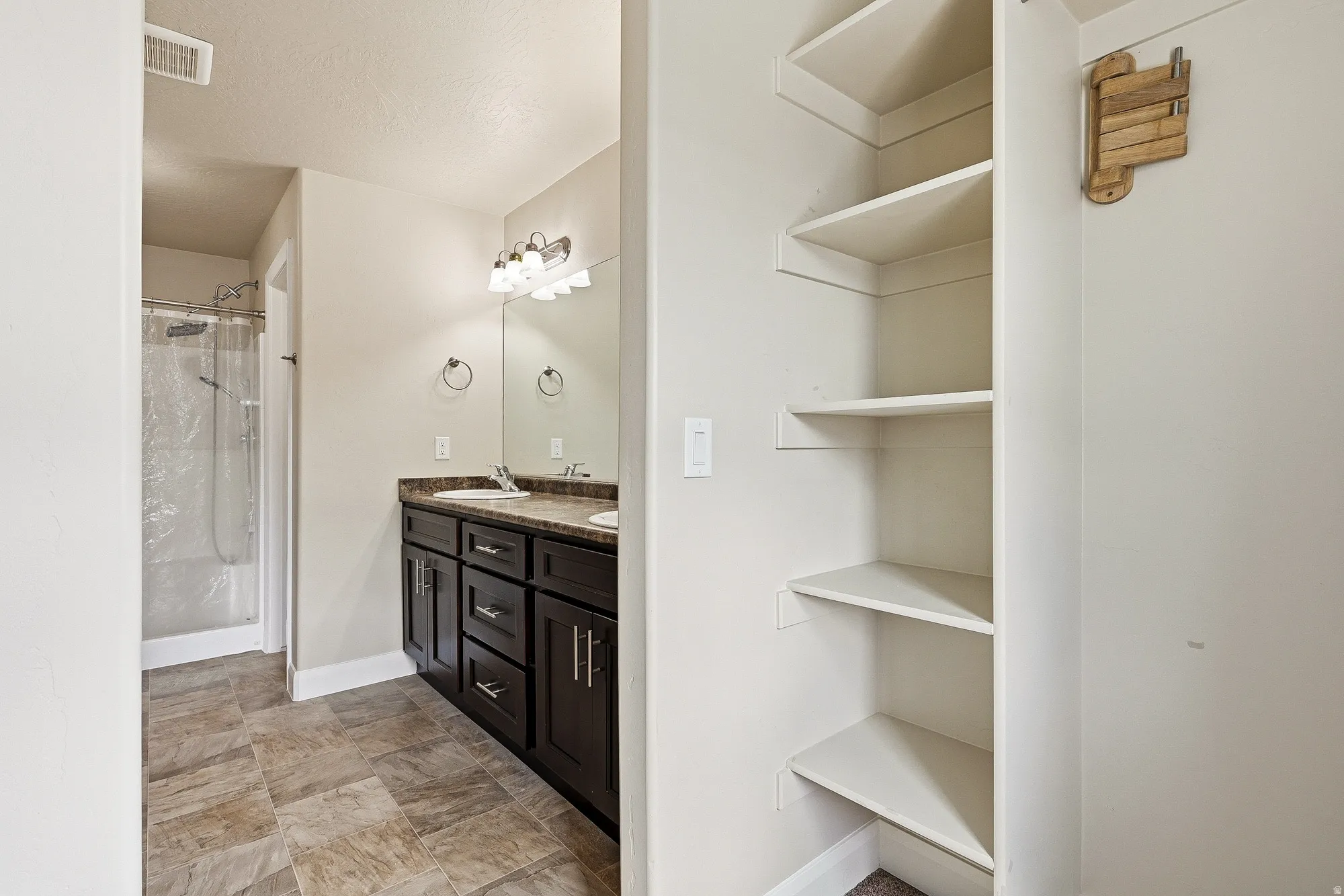 Bathroom with double vanity, a stall shower, a closet, and stone finish floors