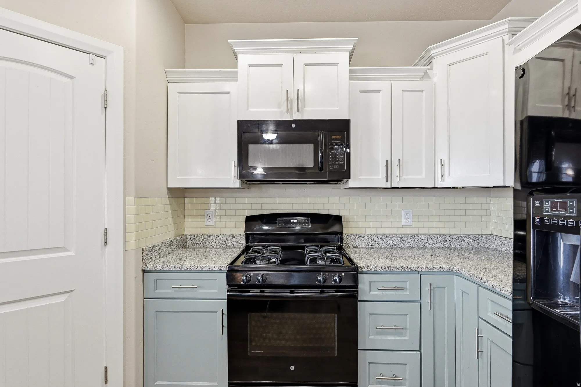 Dual tone kitchen featuring black appliances, light stone countertops, decorative backsplash, and dual tone cabinets