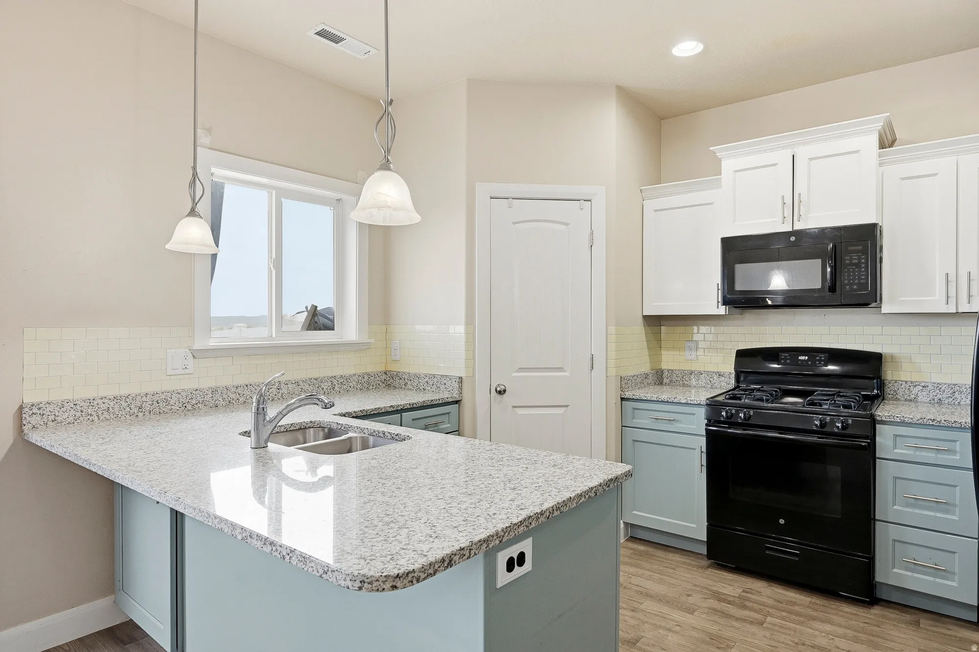Contemporary kitchen featuring a dual-tone cabinetry, light granite countertops, a stainless steel double basin sink, and a four-burner gas range with an overhead microwave