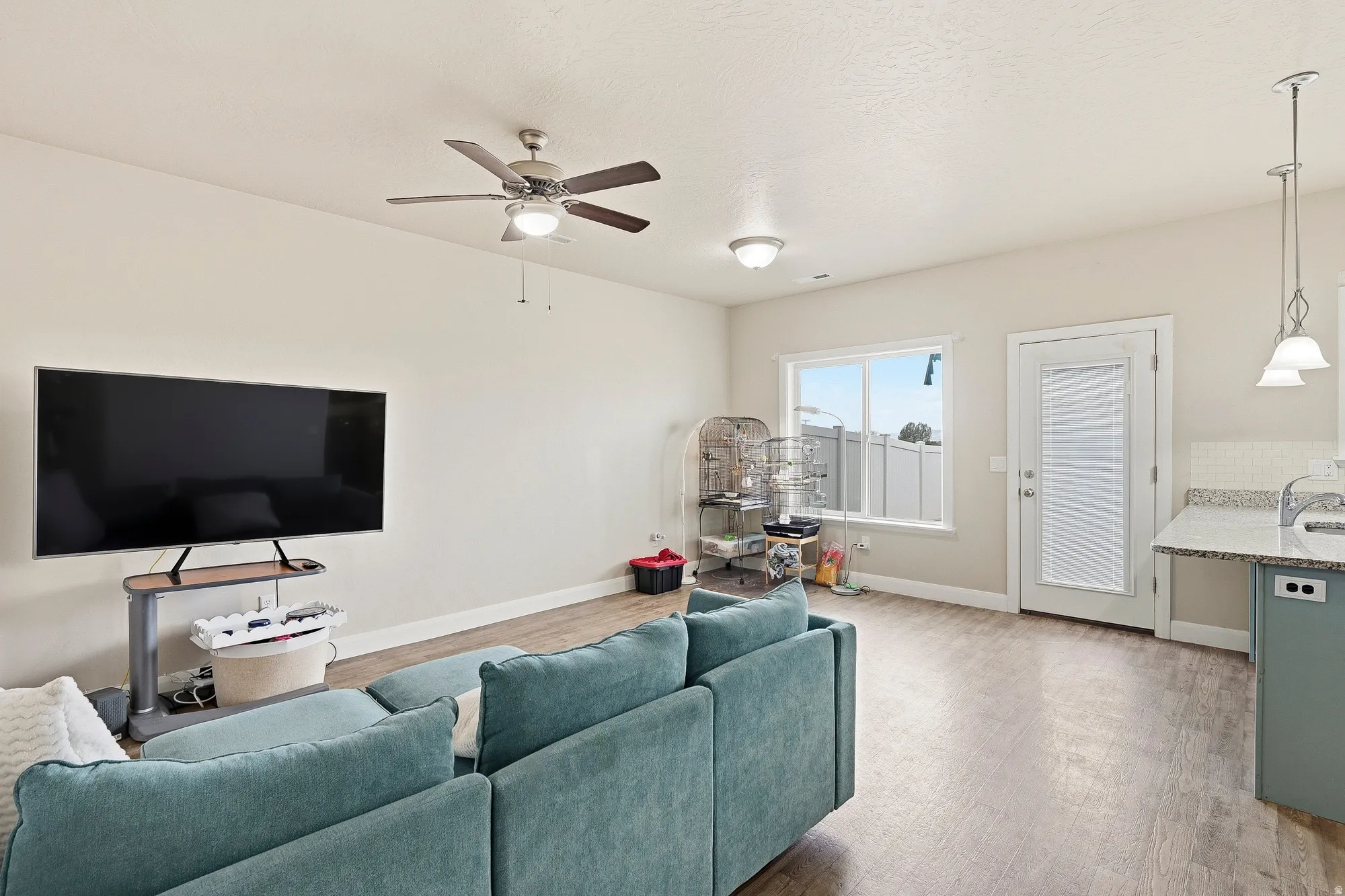 Open-concept living area featuring wood-finish flooring, a ceiling fan with integrated lighting, recessed lighting, and a window providing natural light