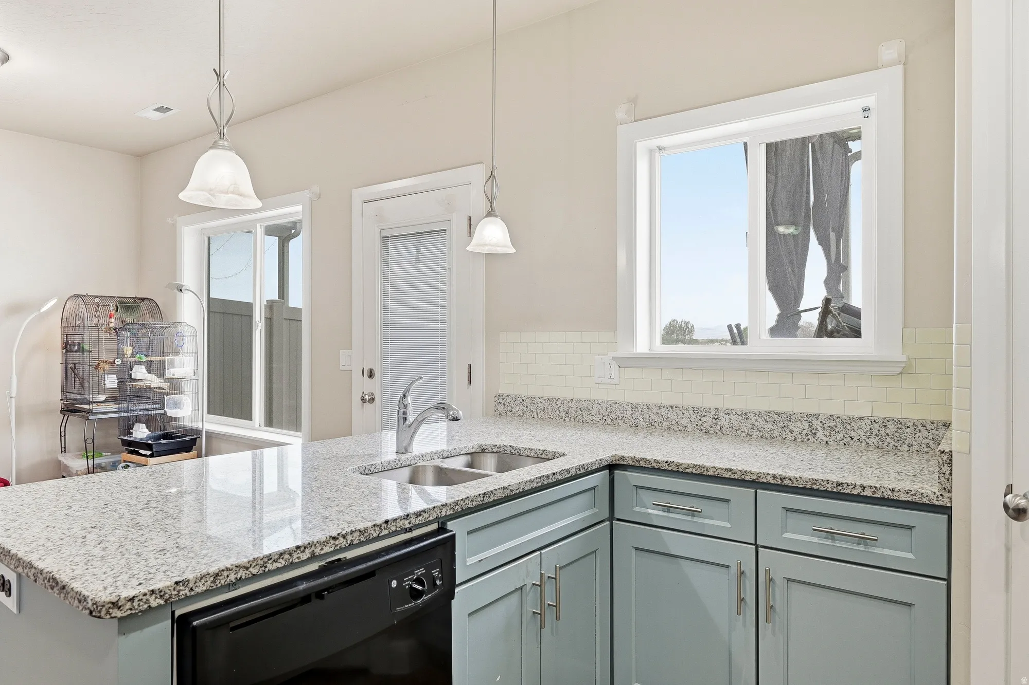 Kitchen featuring light blue cabinetry, speckled countertops, a stainless steel double-basin sink with a chrome faucet, and a subway tile backsplash