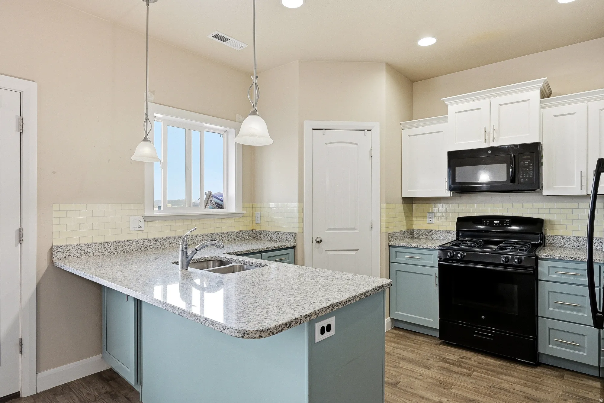 Kitchen with black appliances, light stone countertops, a peninsula, decorative light fixtures, and wood finished floors