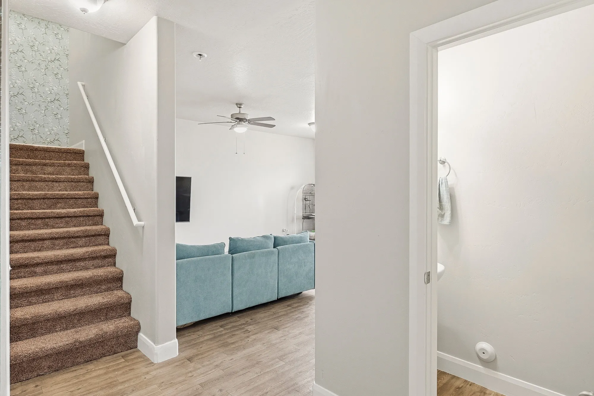 Carpeted staircase with white railing, wood-finish flooring, and a ceiling fan with light fixture