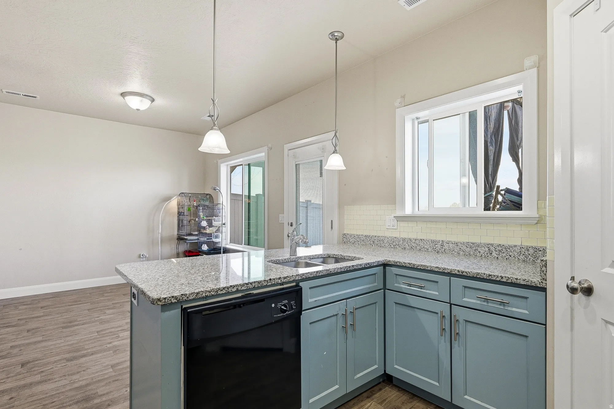 Kitchen with a peninsula, dishwasher, light stone countertops, hanging light fixtures, and dark wood-type flooring