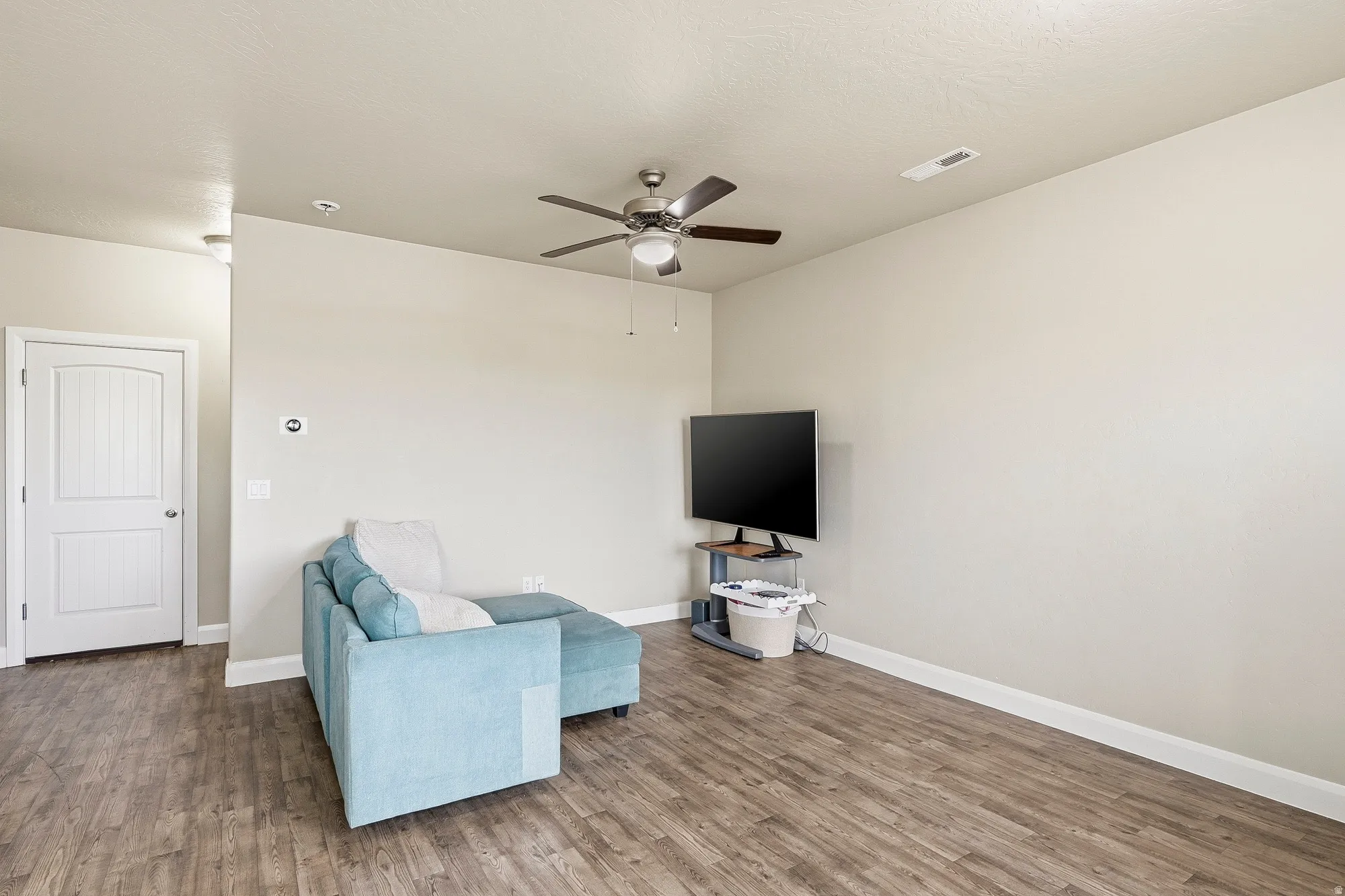 Spacious room featuring wood-finish flooring, light-toned walls, and a ceiling fan