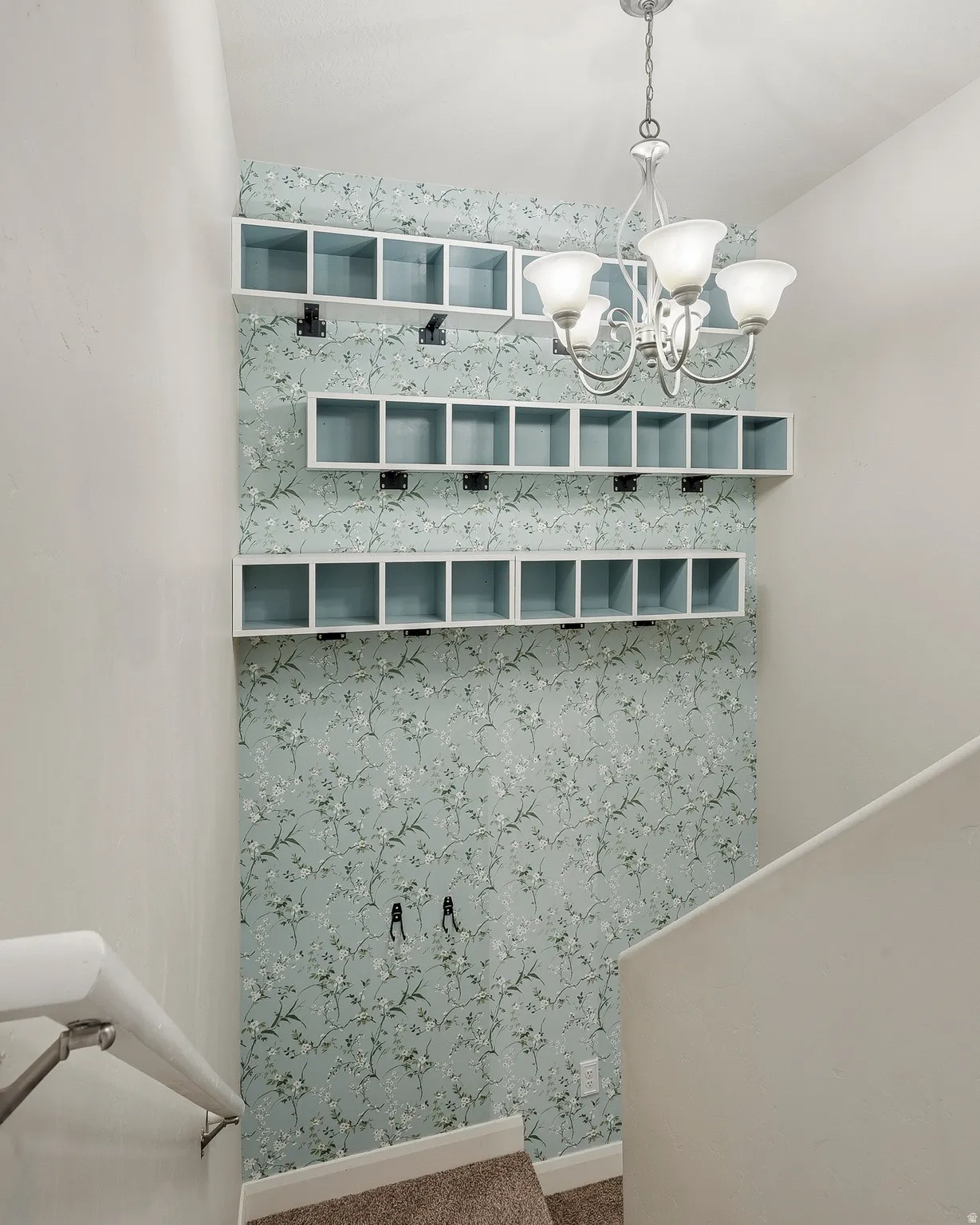 Stairwell featuring custom built-in cubby storage, decorative floral wallpaper, and a multi-light chandelier