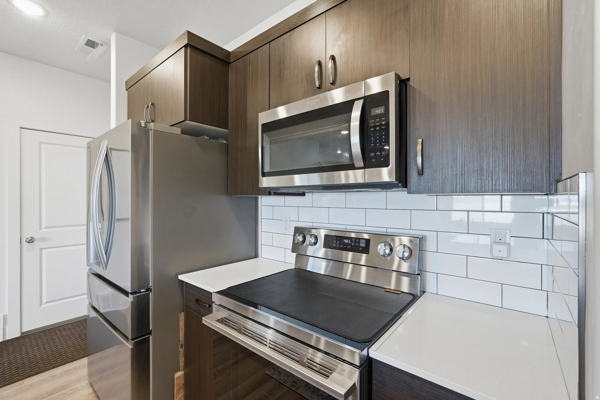 Kitchen with stainless steel appliances, dark wood finish cabinetry, tasteful backsplash, modern cabinets, and light stone countertops