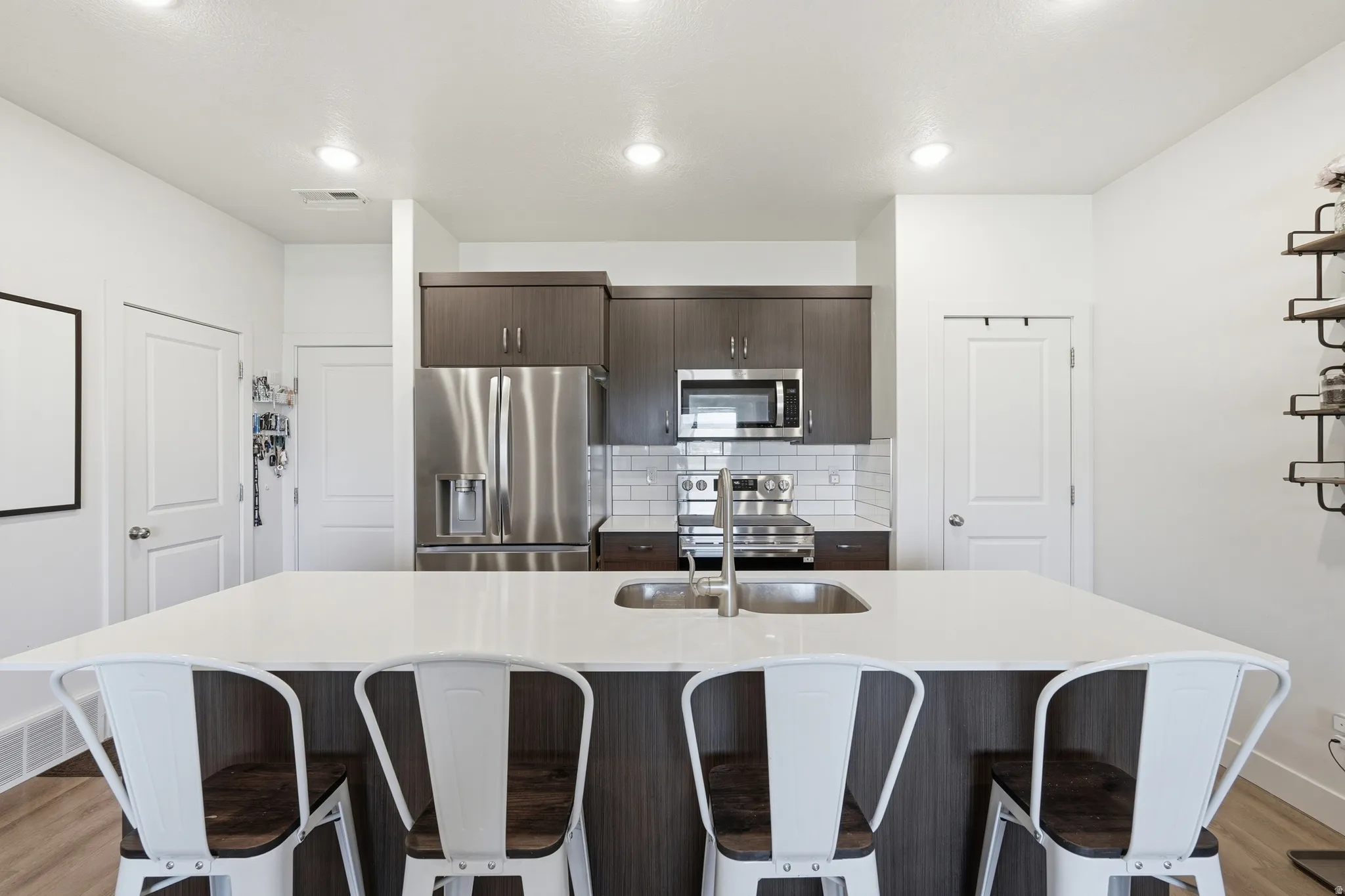 Kitchen featuring light wood-style floors, dark wood finish cabinets, stainless steel appliances, and a kitchen bar
