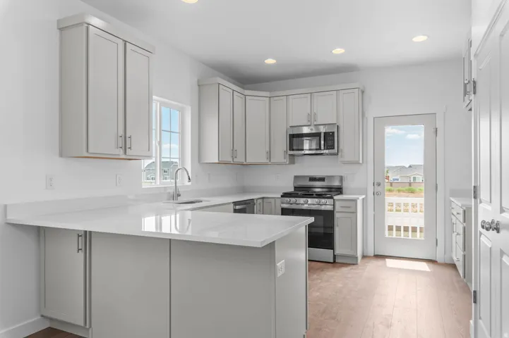 Modern kitchen featuring light wood-finish flooring, white cabinetry with contemporary hardware, stainless steel appliances, and sleek white countertops