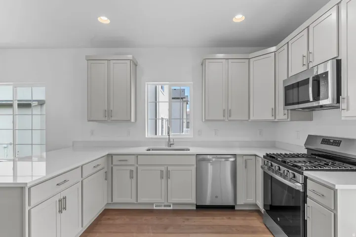 Contemporary kitchen featuring light-toned cabinetry, stainless steel appliances, white countertops, a gas range, and wood-finish flooring