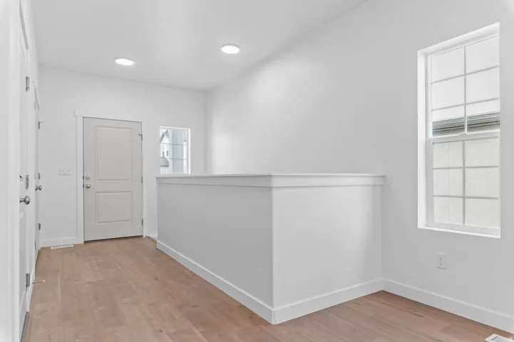 Bright hallway featuring wood-finish flooring, recessed lighting, and a white interior door