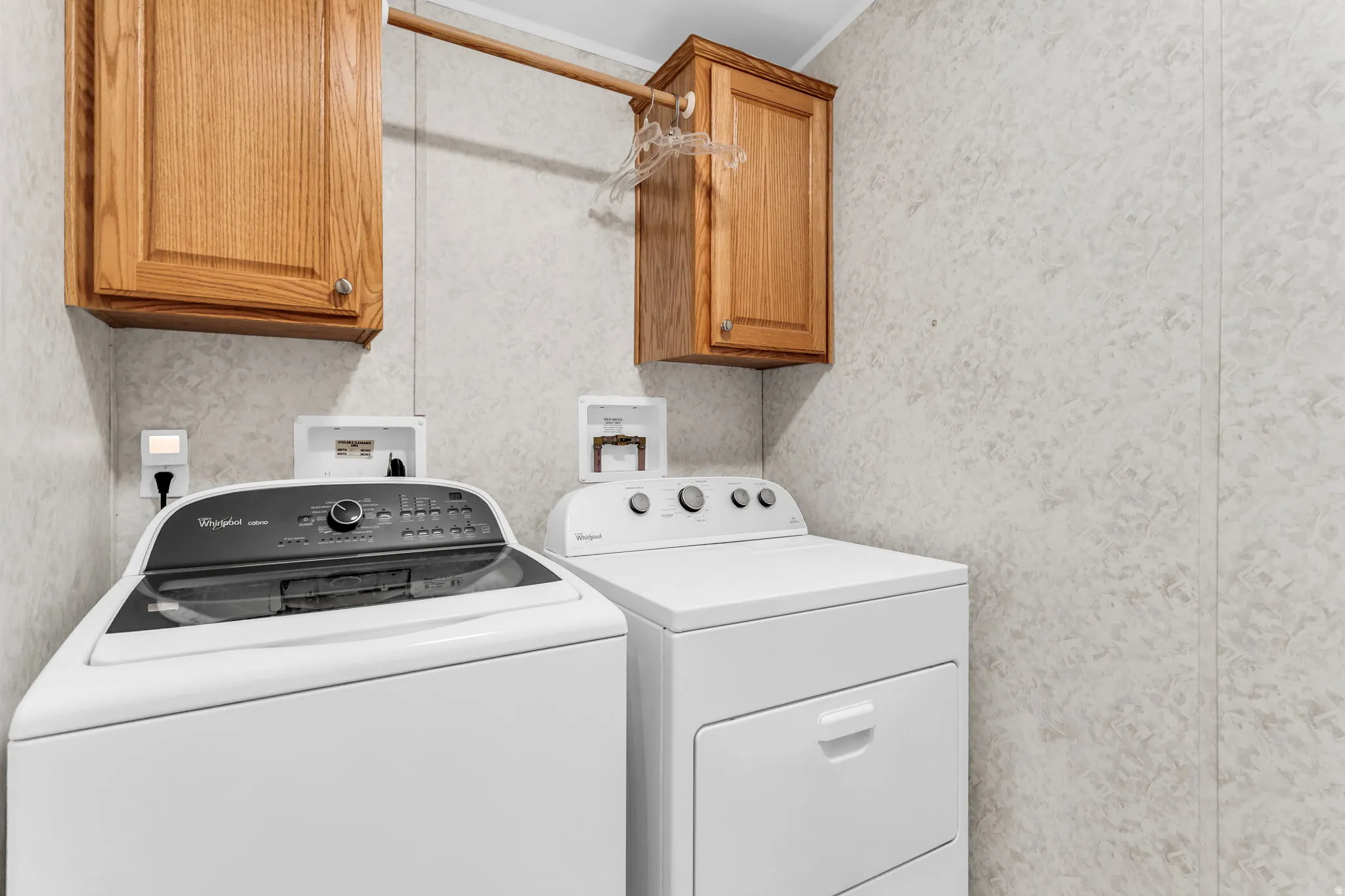 Laundry room featuring wallpapered walls, separate washer and dryer, and cabinet space