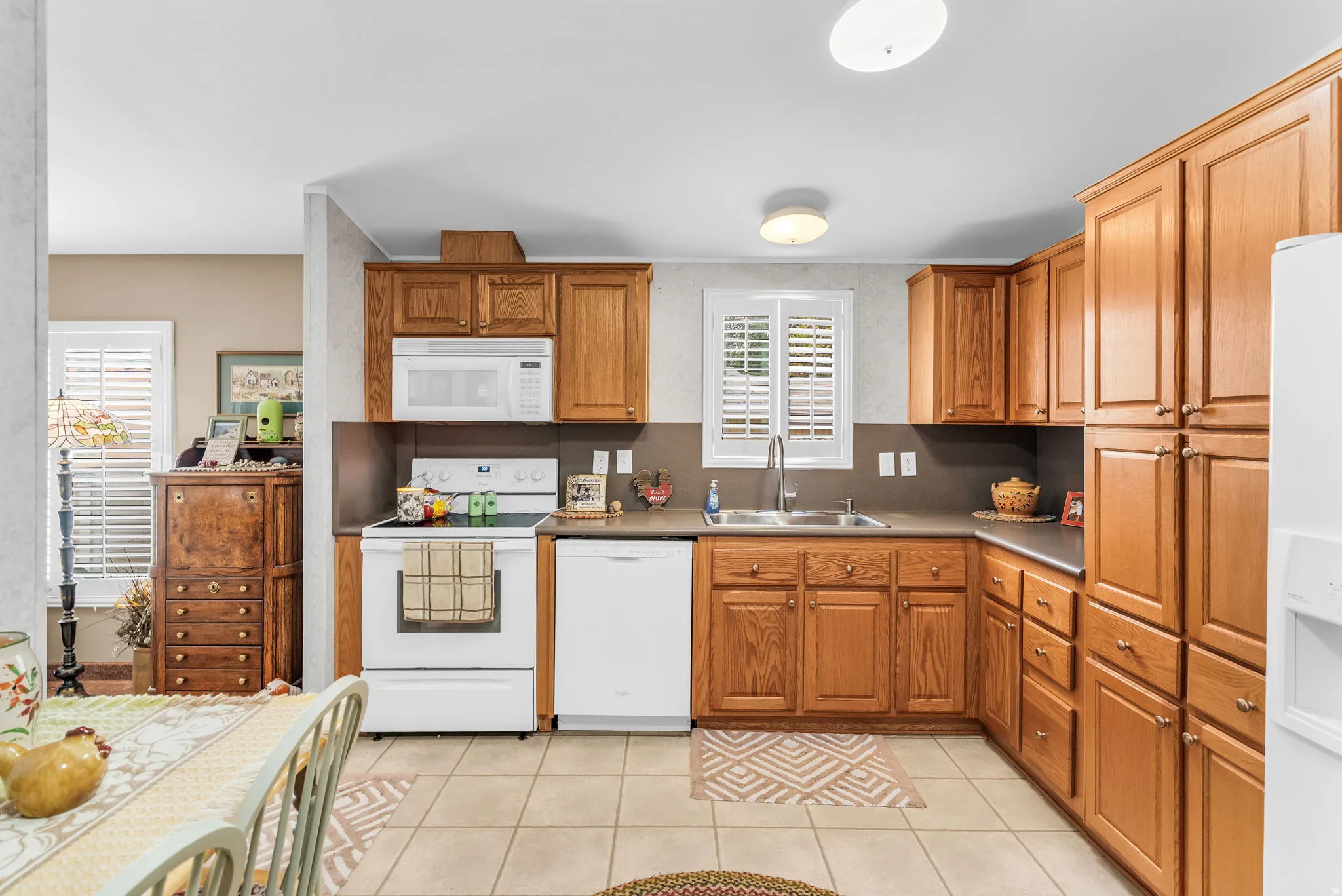 Kitchen featuring white appliances, wood finish cabinetry, light tile patterned floors, and light countertops