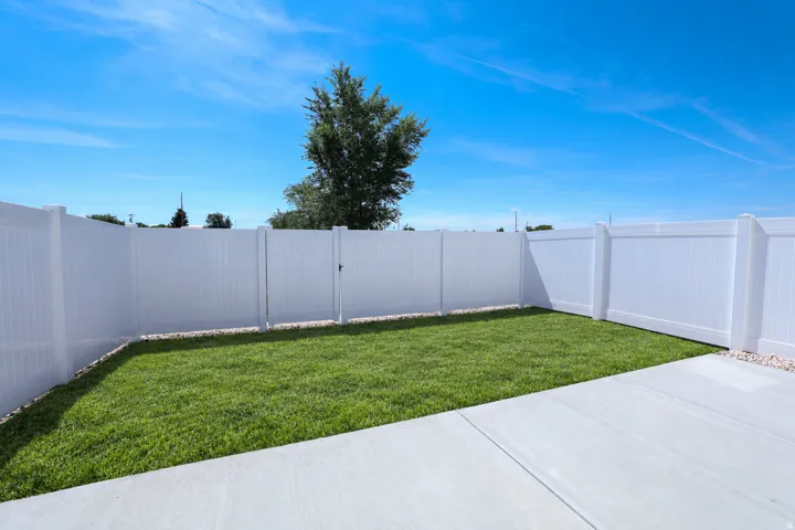 Expansive backyard featuring a manicured lawn, a solid white vinyl fence, and a concrete patio