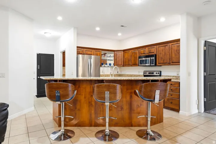 Kitchen featuring a breakfast bar, an island with sink, wood finish cabinetry, stainless steel appliances, and light stone counters