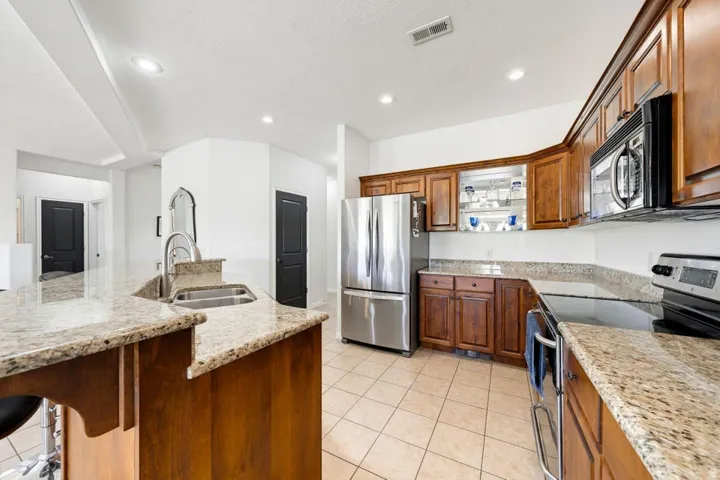 Kitchen featuring stainless steel appliances, light stone countertops, a spacious island, wood finish cabinets, and light tile patterned floors