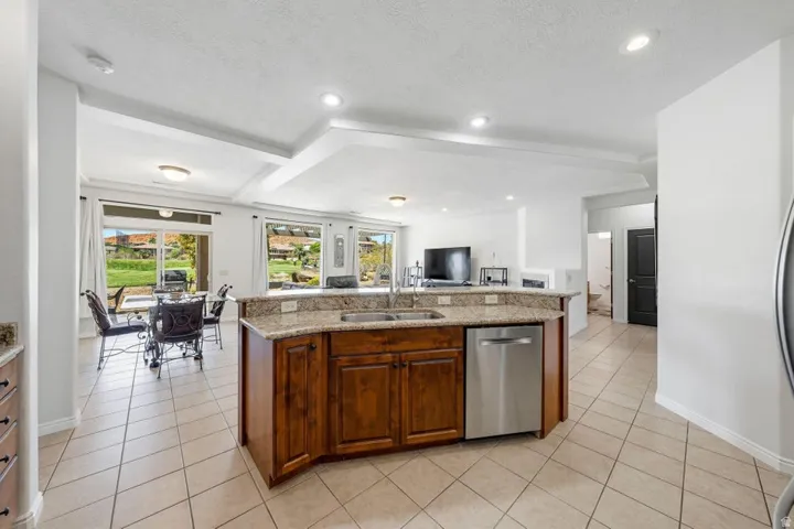 Kitchen with light stone countertops, light tile patterned floors, dishwasher, open floor plan, and a kitchen island with sink